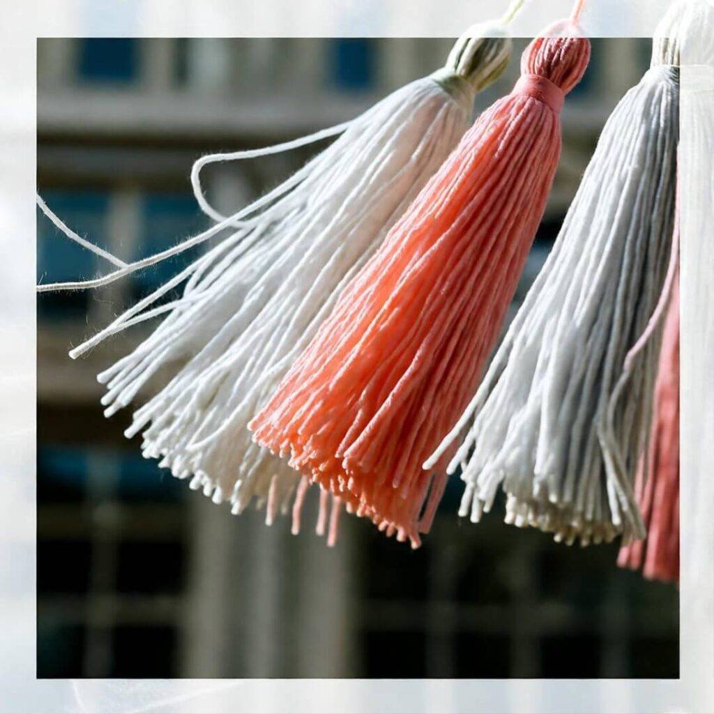 Tassels in white, pink, and coral hang against a blurred building background.