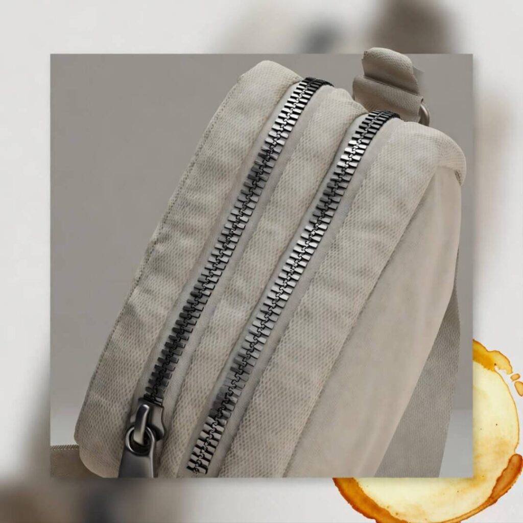 Tilted close-up of mini crossbody with wonky zippers, coffee stain smudge.