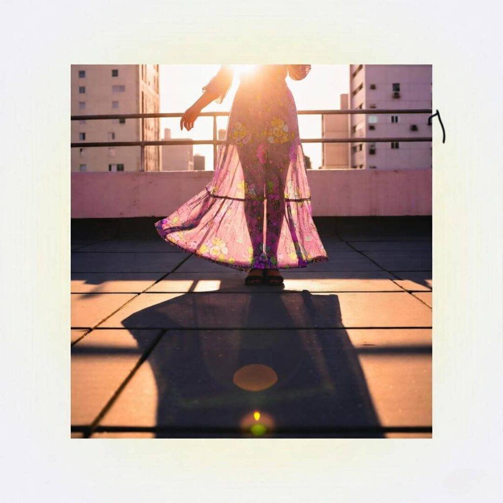 Woman in floral maxi dress on rooftop, sunset shadows, pinks and yellows pop.