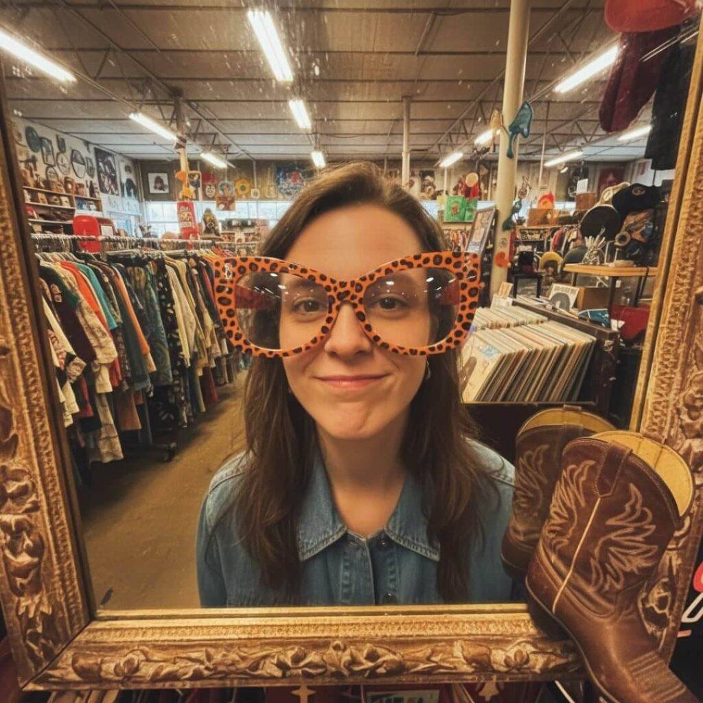 Reflection in warped mirror, leopard-print specs, cowboy boot, Austin thrift store.